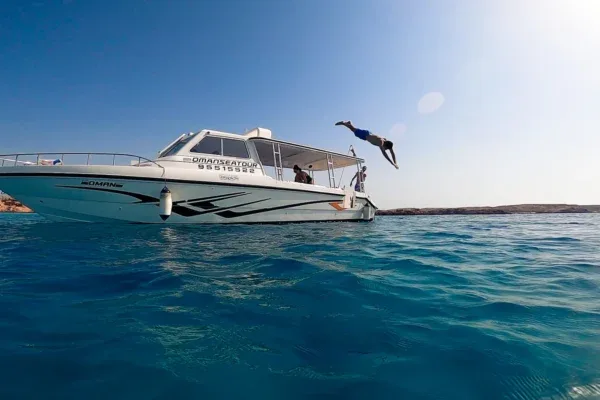 Une personne plonge d'un bateau blanc en mer, ciel bleu clair