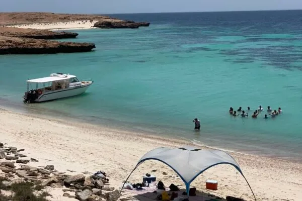 Plage de sable clair avec des baigneurs et un bateau amarré