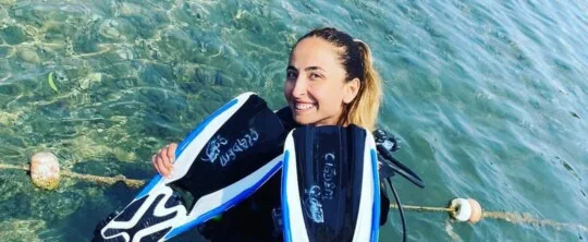 Jeune femme souriante tenant des palmes de plongée dans l'eau