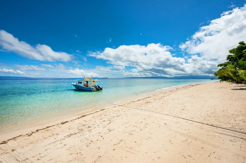 Plage de sable blanc, mer turquoise et petit bateau de pêche