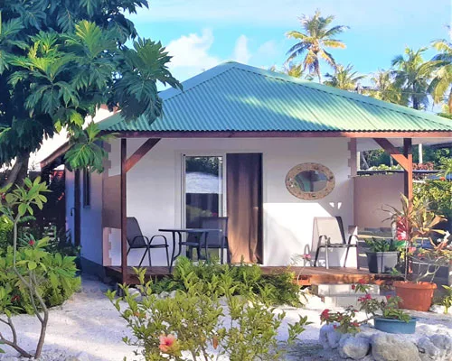 Petite maison blanche avec toit vert, terrasse et végétation tropicale