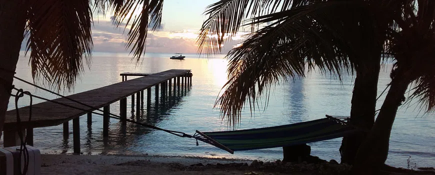 Plage tropicale avec ponton en bois et hamac au coucher du soleil