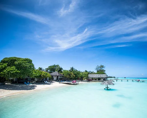 Plage de sable blanc, bâtiments du centre, eau turquoise et ciel bleu