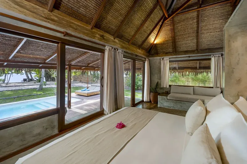 Chambre avec lit, vue sur piscine et plage tropicale ensoleillée
