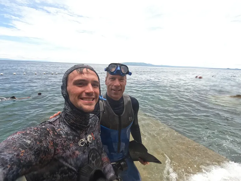 Deux plongeurs souriants posent sur un ponton au bord de la mer