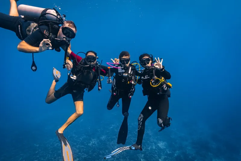 Quatre plongeurs souriants et équipés flottent dans l'eau bleue