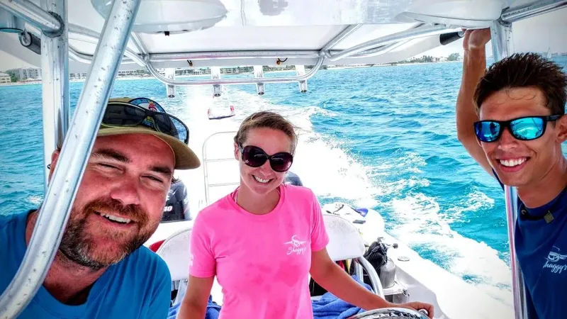 Trois personnes souriantes sur un bateau en mer, lunettes de soleil