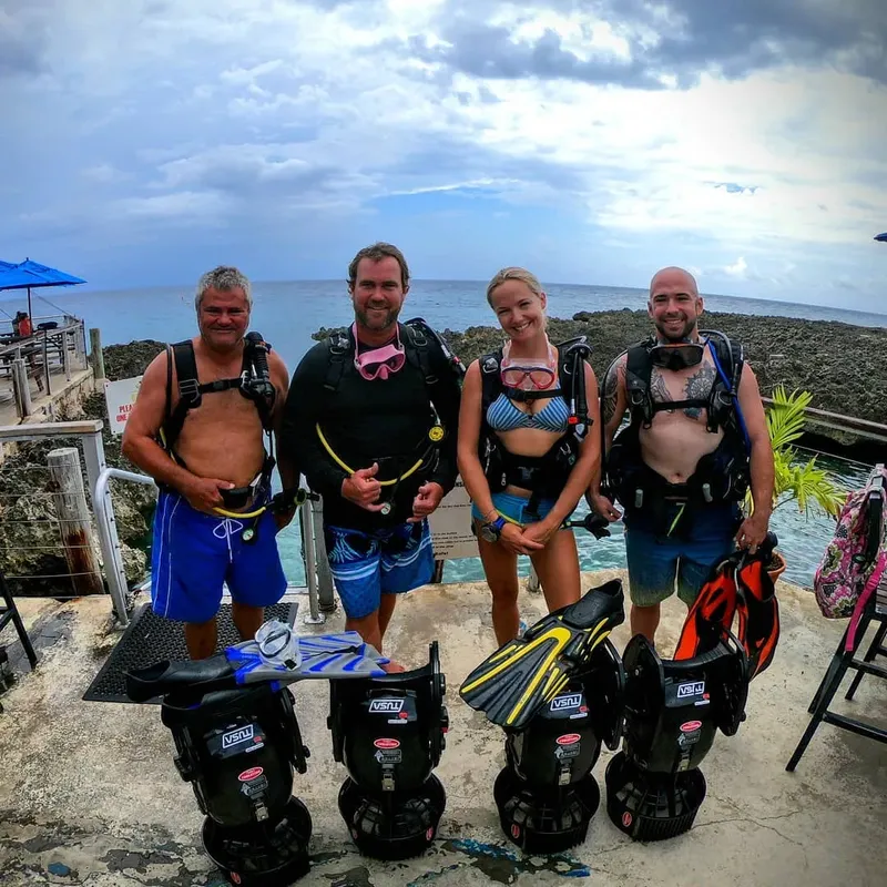 Quatre plongeurs équipés posent devant des scooters sous-marins sur un quai