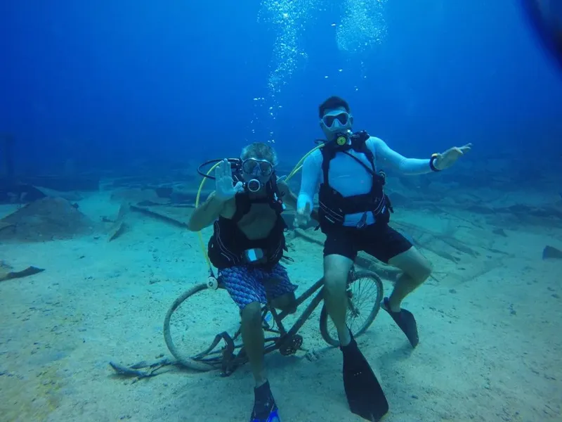 Deux plongeurs sourient devant un vélo immergé dans l'eau