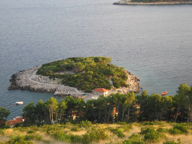 Île rocheuse avec bâtiments, embarcations et végétation côtière ensoleillée
