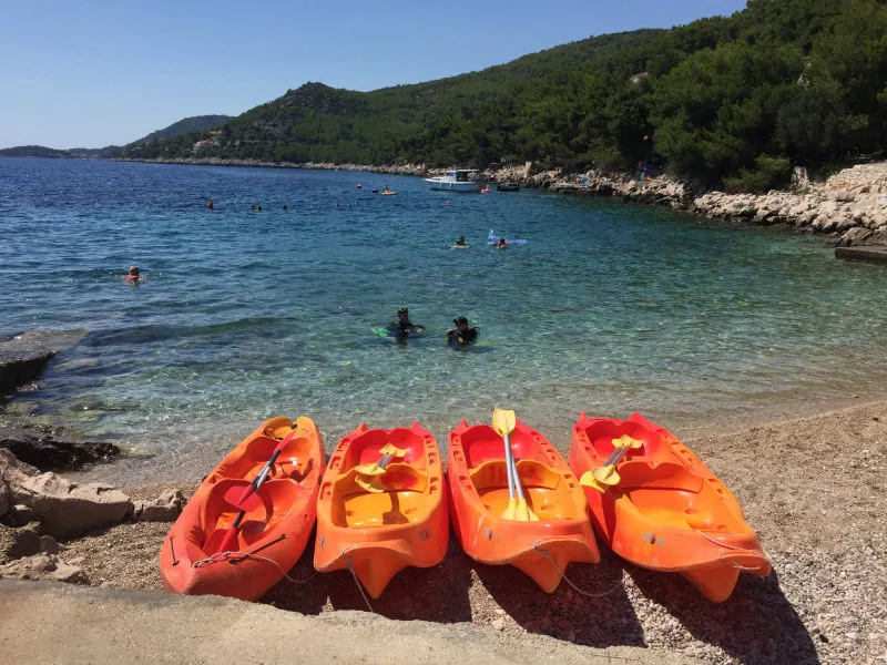 Personnes dans l'eau, kayaks sur une plage de galets ensoleillée