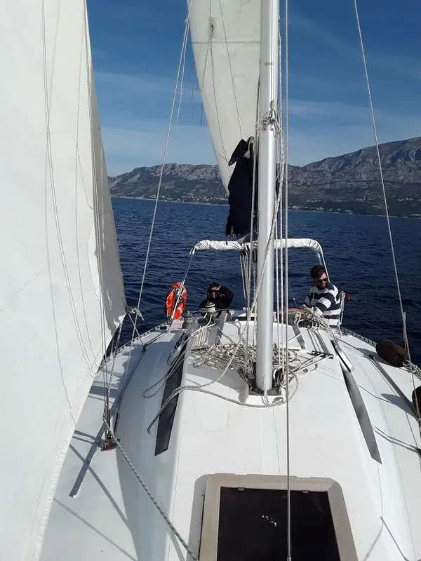 Voilier en mer avec deux personnes à bord, paysage montagneux