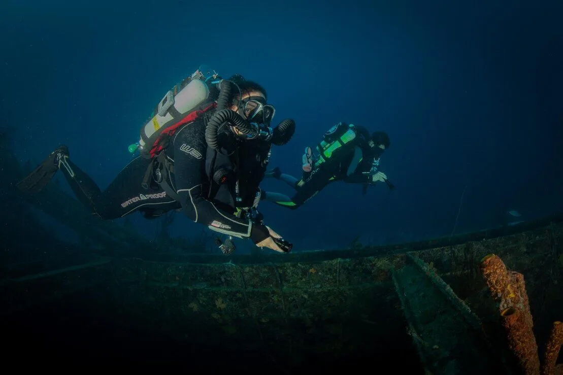 Deux plongeurs explorent un épave sous-marine dans l'eau bleue