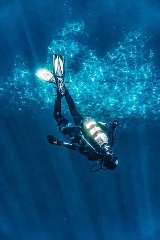 Plongeur en combinaison noire nageant dans une eau bleue claire