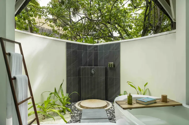 Salle de bain extérieure avec douche et baignoire, végétation luxuriante