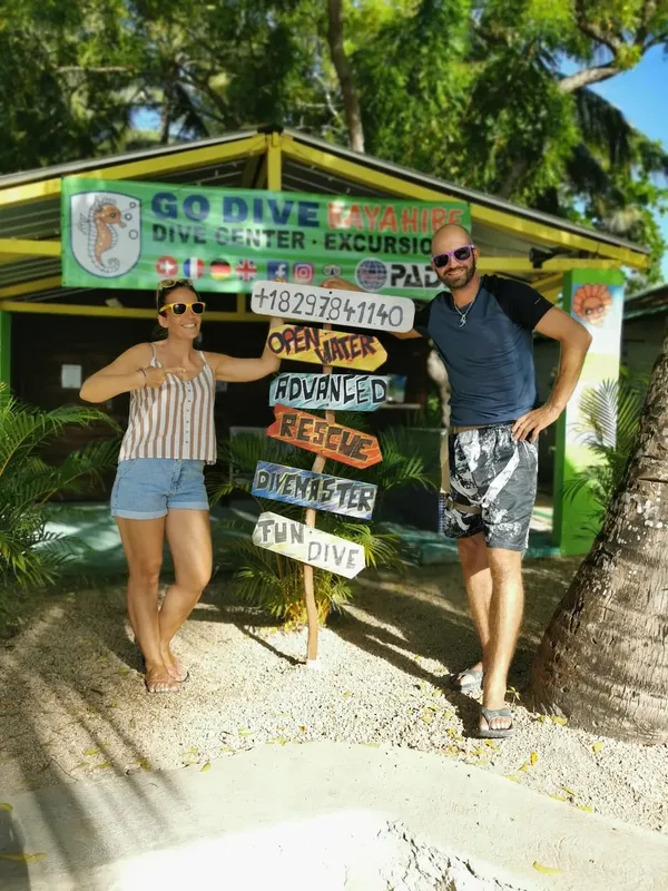 Deux personnes souriantes devant l'enseigne d'un centre de plongée tropical