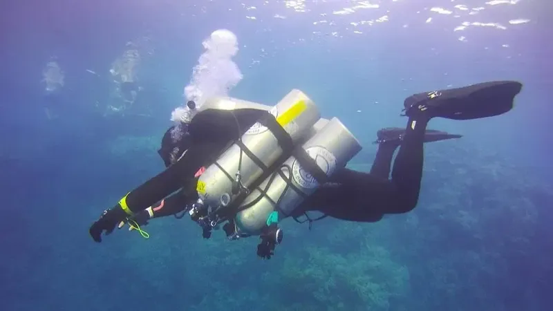 Plongeur en combinaison noire avec plusieurs bouteilles sous l'eau