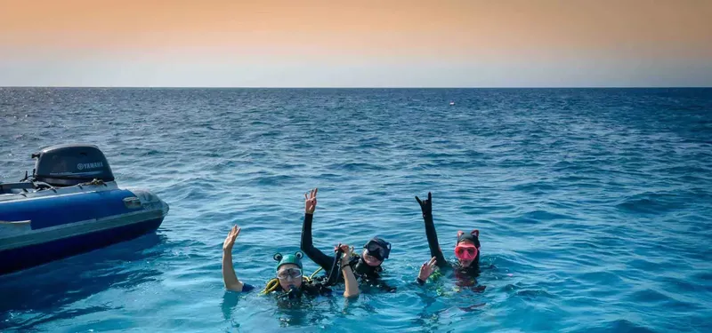 Trois plongeurs souriants flottent à la surface près d'un bateau
