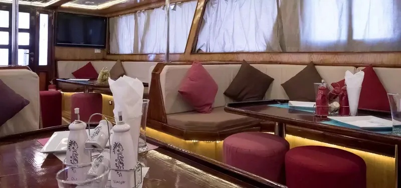 Intérieur d'un bateau de plongée avec tables, banquettes et coussins rouges