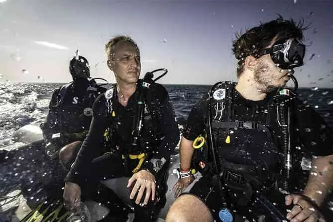 Trois plongeurs en combinaison sur un bateau en pleine mer