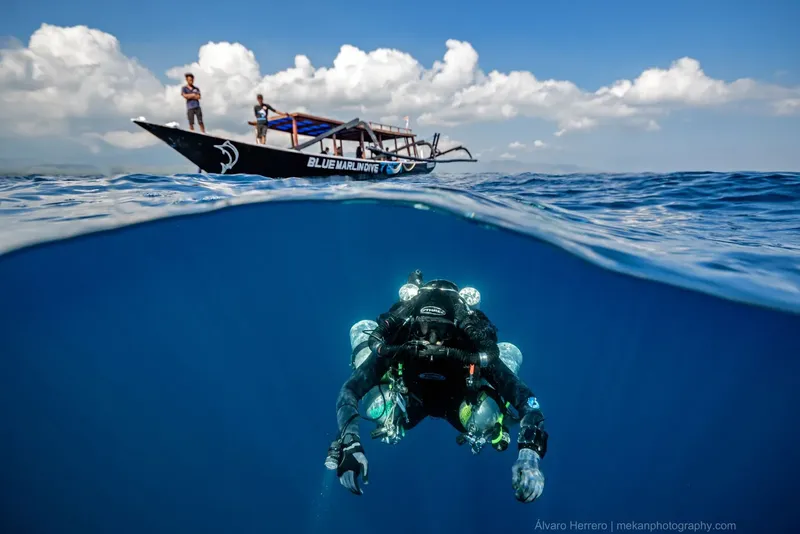 Plongeur en pleine eau avec bateau traditionnel et ciel nuageux