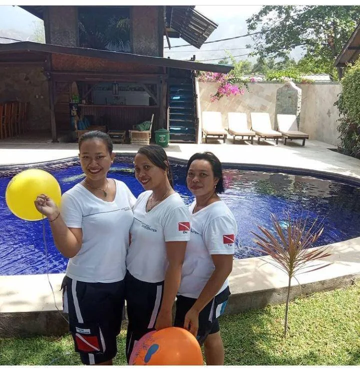Trois femmes souriantes posent devant une piscine et un abri