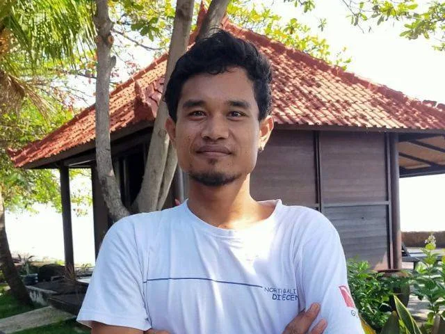 Portrait d'un homme souriant devant un petit bâtiment en bois