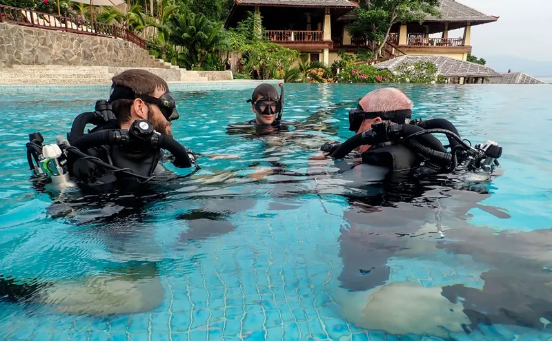 Trois plongeurs en combinaison discutent dans une piscine turquoise