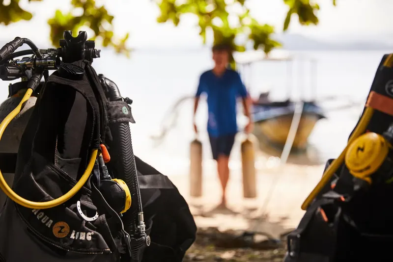 Equipement de plongée au premier plan, un plongeur se dirige vers un bateau