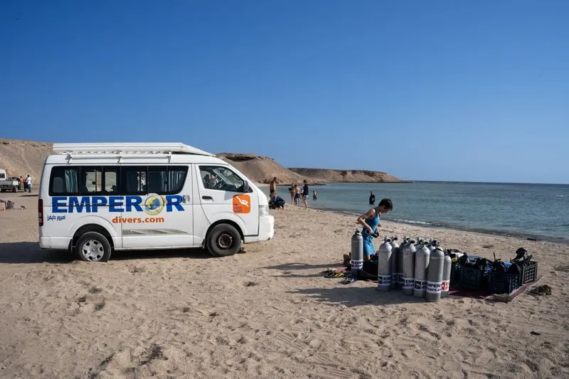 Plage ensoleillée avec van, bouteilles de plongée et personnes préparant l'équipement
