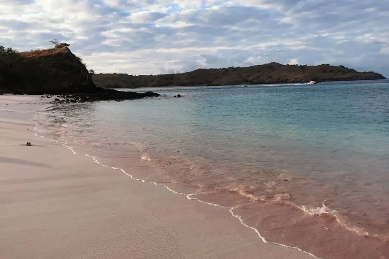Plage de sable rose avec mer turquoise et quelques bateaux au loin