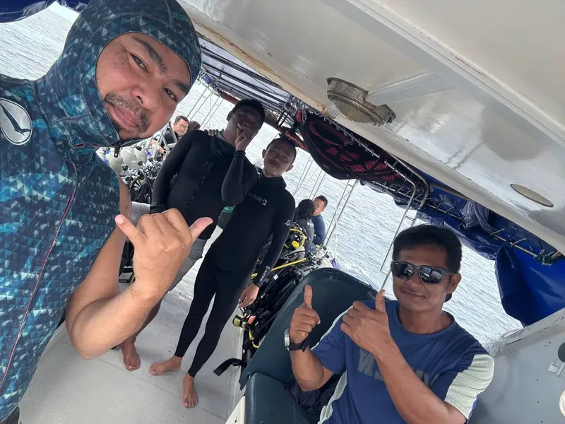 Trois plongeurs souriants font des signes positifs sur un bateau