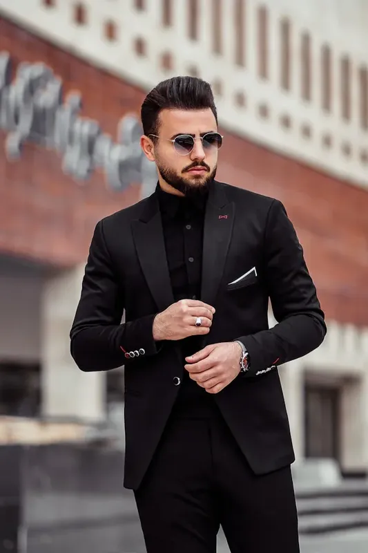 Un homme en costume noir et lunettes de soleil pose en ville