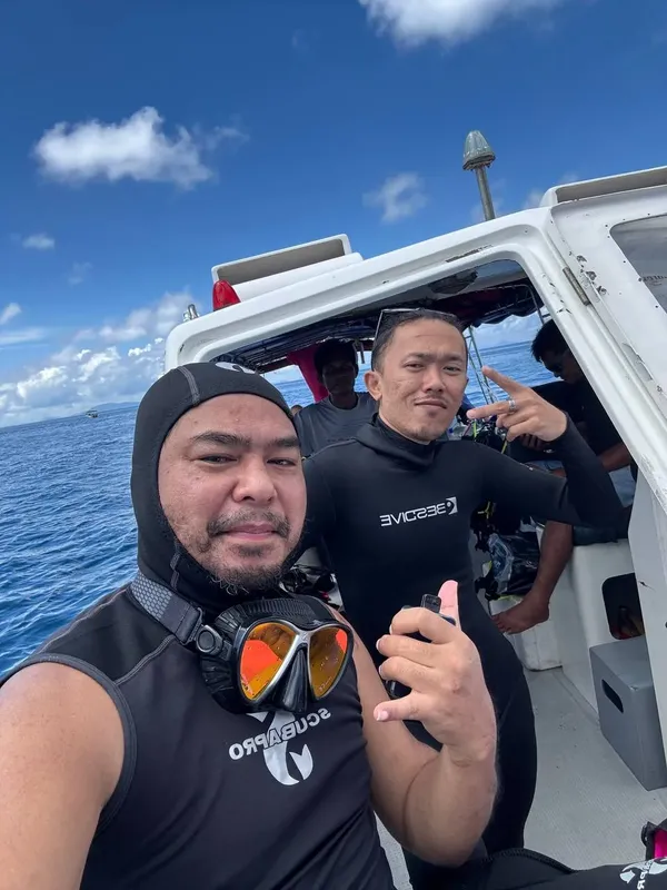 Deux plongeurs souriants sur un bateau en mer, équipés de masques