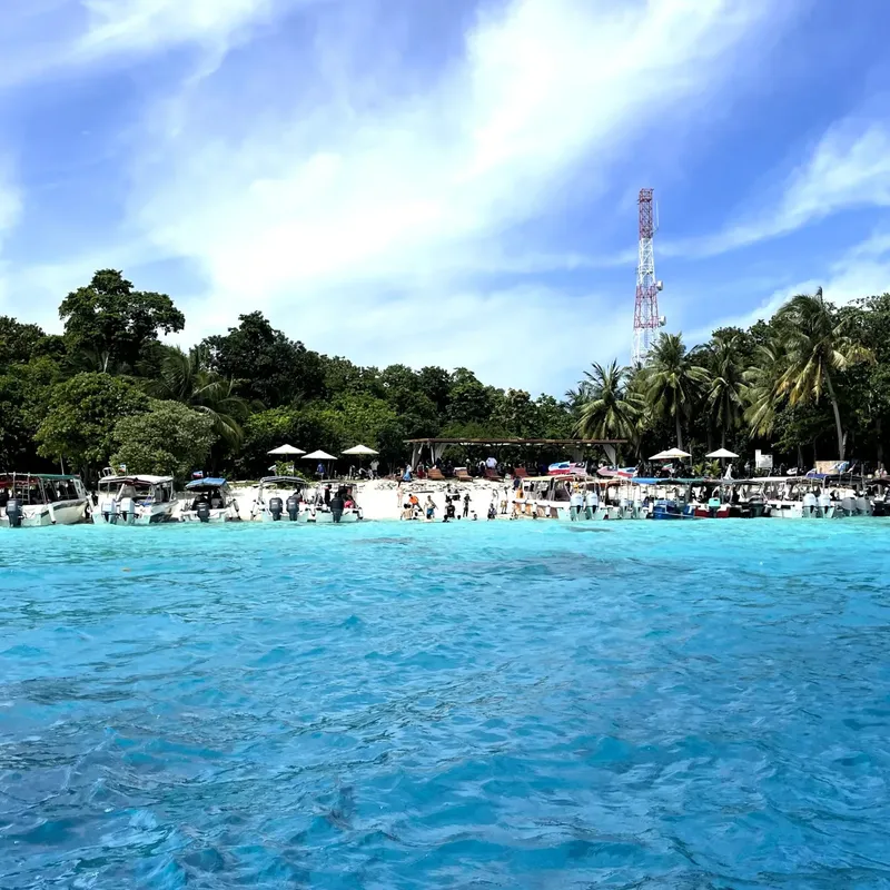 Plage tropicale avec bateaux, personnes et végétation luxuriante sous ciel bleu