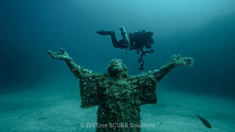Plongeur au-dessus d'une statue sous-marine colonisée par la vie marine