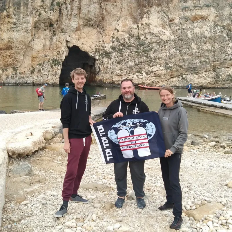 Trois personnes souriantes posent avec un drapeau de plongée technique