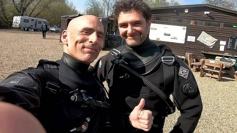 Deux plongeurs souriants en combinaison, devant un bâtiment du centre