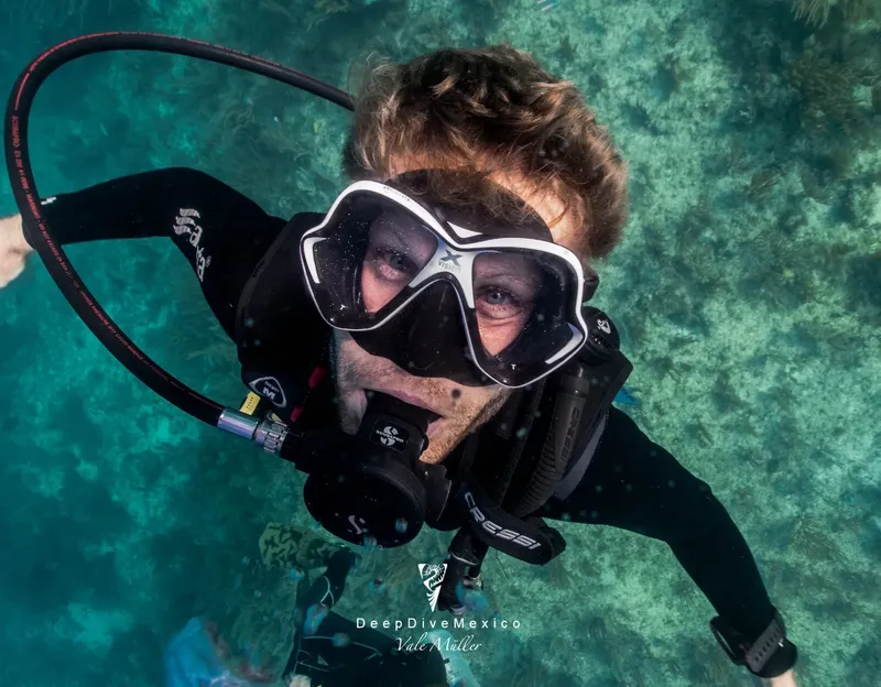 Plongeuse souriante avec masque et détendeur, regardant la caméra sous l'eau