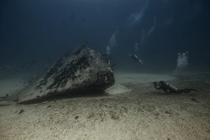 Plongeurs explorant un épave sous-marine dans un environnement sablonneux