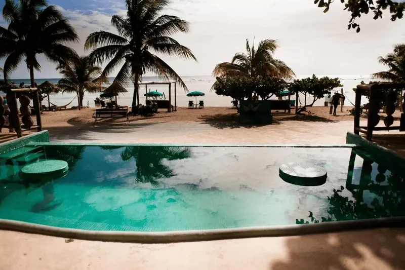 Vue d'une plage avec des personnes, des palmiers et une piscine turquoise