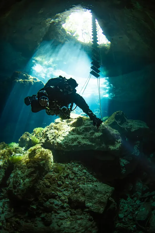 Plongeur explore une grotte sous-marine éclairée par un rayon de soleil