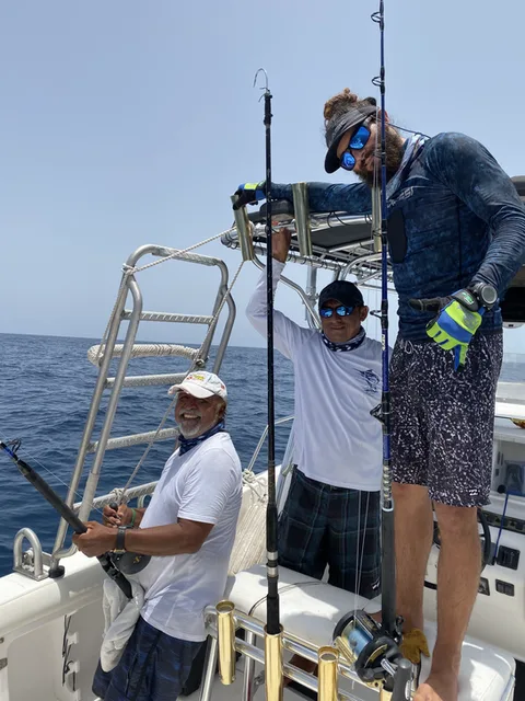 Trois hommes souriants sur un bateau en mer, pêchant au gros