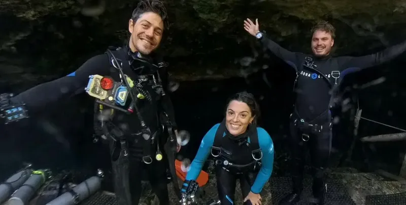 Trois plongeurs souriants posent sous l'eau avec leur équipement