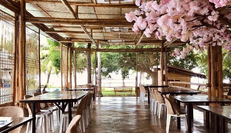 Terrasse ombragée avec tables et chaises, vue sur la mer et végétation