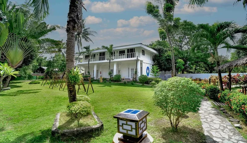 Bâtiment blanc entouré de végétation tropicale et d'une pelouse verte soignée