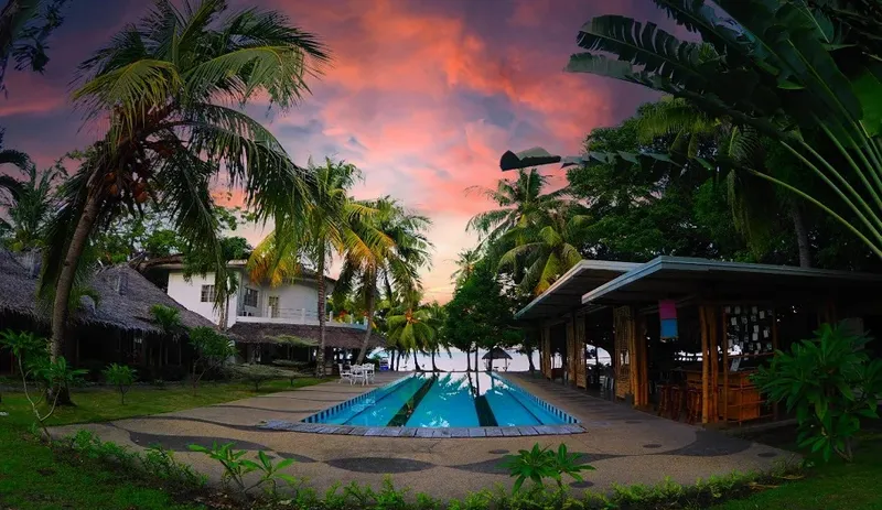 Bâtiments du centre de plongée, piscine et végétation tropicale au coucher du soleil