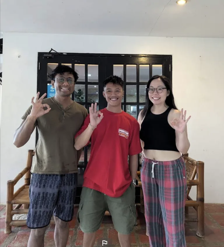 Trois jeunes adultes souriants font des signes devant une porte