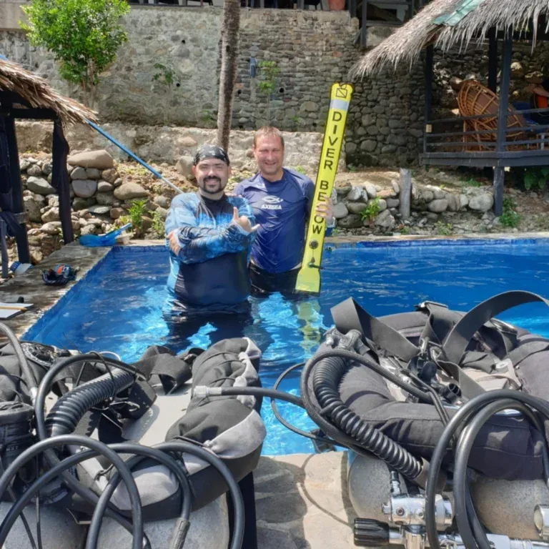 Deux plongeurs souriants dans une piscine avec du matériel autour