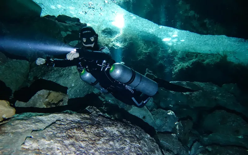 Plongeur explore une grotte sous-marine avec deux bouteilles et lampe
